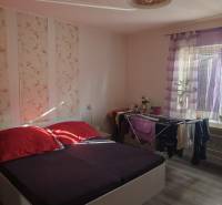 Na predaj 3-izb. rodinný dom, Gabčíkovo – Polná ulica - Spálňa v rodinnom dome s posteľou, dekoratívnou tapetou a podlahou s dreveným dekorom.