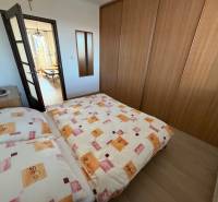 3 izbový byt s balkónom Topoľčany  - Spálňa v 3-izbovom byte s posteľou, vstavanou skriňou a podlahou s dreveným dekorom.