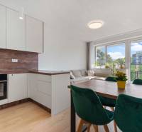 | Krásny a moderný 2-izbový byt | 51,50m² | - Svetlá kuchyňa s obývačkou, drevený dekor, jedálenský stôl a zelené stoličky v 2-izbovom byte.
