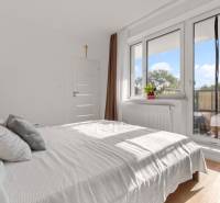 | Krásny a moderný 2-izbový byt | 51,50m² | - Svetlá spálňa v 2-izbovom byte s posteľou, balkónom a podlahou s dreveným dekorom.