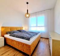 Posledný investičný krásny 2-izbový byt | 55 m² | RÍNOK RAČA - Spálňa s pohodlnou posteľou, lampou a komodou v 2-izbovom byte, podlaha s dreveným dekorom.