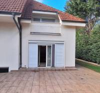 Luxusný rodinný dom s bazénom a dvojgarážou v Komárne - Rodinný dom v Komárne s terasou, záhradou a bielymi okenicami.