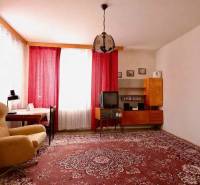 RD v jednej z najžiadanejších lokalít Michaloviec – pod Hrádkom - Obývačka v rodinnom dome s červeným kobercom, kreslom a závesmi na oknách.