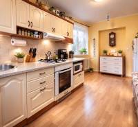 REZERVONY - 2 izbový tehlový byt na Novej Dubnici, 60  - Kuchyňa v 2-izbovom byte s podlahou s dreveným dekorom, svetlá linka a rastliny.