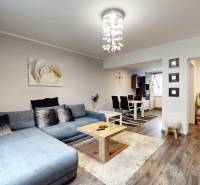 Prerobený rodinný dom na veľkom tichom pozemku v obci Pruské   - Obývacia izba s podlahou s dreveným dekorom, sivou sedačkou a jedálenským stolom v rodinnom dome.