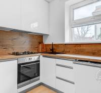 Slnečný 2i byt, pivnica, internet v cene, Nivy, Niťová ul. - Kuchyňa s bielymi skrinkami, spotrebičmi a podlahou s dreveným dekorom v 2-izbovom byte.