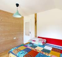 3D, Predaj novostavba, celoročne obývateľná chata, Stupava, Ovocinár - Izba s drevenými stenami, farebnou posteľou, skriňou a svetlom v Chate.