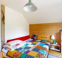 3D, Predaj novostavba, celoročne obývateľná chata, Stupava, Ovocinár - Spálňa v chate s farebnou prikrývkou, dreveným obkladom a policou.