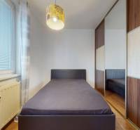 3-izbový byt s extrémne nízkymi nákladmi v Michalovciach - Jednolôžková posteľ pri okne, vstavaná skriňa a podlaha s dreveným dekorom v 3-izbovom byte.