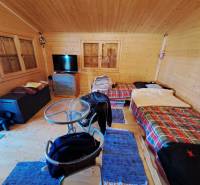 Predáme záhradu so zrubovou chatou, Nitra - Dolné Krškany - Izba v Záhradách so stolíkom, stoličkami a dvomi posteľami s farebnými prikrývkami.