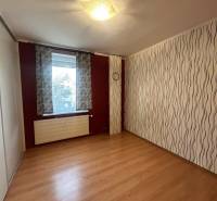 Predaj 3 izb. bytu s balkónom v NZ - Izba v 3-izbovom byte s podlahou s dreveným dekorom a vlnitými tapetami.