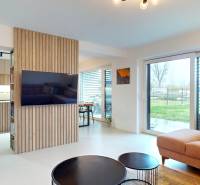 Novozariadený rodinný dom s veľkými spálňami i šatníkom pri Trenčíne   - Obývacia izba s veľkými oknami, pohodlnou sedačkou a dreveným dekorom na stene.