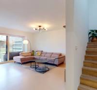 Novozariadený rodinný dom s veľkými spálňami i šatníkom pri Trenčíne   - Interiér rodinného domu: pohovka, knižnica, schody s podlahou s dreveným dekorom a rastlina.