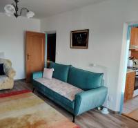 2 izbový byt na Severe - Obývacia izba v 2-izbovom byte s pohovkou a kreslom, podlaha s dreveným dekorom.