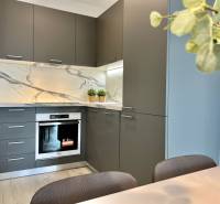 KOMPLETNE ZARIADENÝ SVETLÝ 2-IZB. BYT, NOVOSTAVBA NUPPU, HRANIČNÁ UL. - Kuchyňa v 2-izbovom byte s kamenným obkladom a sivými skrinkami.