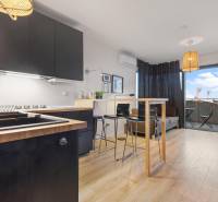 - PREDAJ - APARTMÁN - 38 m2 + 14 m2 LOGGIA - TEHELNÉ POLE - Kuchyňa s čiernymi skrinkami, barovým pultom a podlahou s dreveným dekorom v 1-izbovom byte.