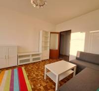 Prenájom 2-izbového bytu v Poprade na Dostojevského ul. - Obývacia izba s bielymi skrinkami, sivou sedačkou a podlahou s dreveným dekorom v 2-izbovom byte.