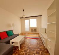 Prenájom 2-izbového bytu v Poprade na Dostojevského ul. - Obývacia izba v 2-izbovom byte s pohovkou, bielym nábytkom, pestrofarebnými vankúšmi a podlahou s dreveným dekorom.