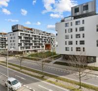 BA/PETRŽALKA-Prenájom 1i bytu s klimatizáciou a balkónom - Slnečnice - Petržalka: Biele obytné budovy s parkovacími miestami na ulici a modrou oblohou.