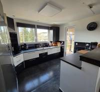 Zabehnutá novostavba: Komfort domu, pokoj vidieka a na skok do BB a ZV - Kuchyňa v rodinnom dome s keramickou podlahou, tmavým nábytkom a veľkými oknami.