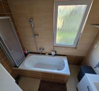 Zabehnutá novostavba: Komfort domu, pokoj vidieka a na skok do BB a ZV - Kúpeľňa v rodinnom dome s vaňou a oknom, obložená hnedými kachličkami.