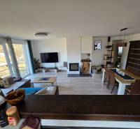 Zabehnutá novostavba: Komfort domu, pokoj vidieka a na skok do BB a ZV - Obývacia izba v rodinnom dome so sedačkou, televízorom a jedálenským stolom na podlahe s dreveným dekorom.