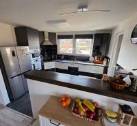 Zabehnutá novostavba: Komfort domu, pokoj vidieka a na skok do BB a ZV - Kuchyňa v rodinnom dome s modernými spotrebičmi, pultom a ovocím na stole.