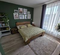 Zabehnutá novostavba: Komfort domu, pokoj vidieka a na skok do BB a ZV - Spálňa v rodinnom dome s podlahou s dreveným dekorom, zelenou stenou a kvetmi.