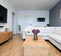 Rezervované -  3i byt v Nemšovej s loggiou po rekonštrukcii - 74m²  - Obývačka v 3-izbovom byte s bielym gaučom, podlahou s dreveným dekorom a dekoráciami.