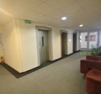 PRENÁJOM kancelárie 27 m2 - Technopol, Kutlíkova ul. - Interiér kancelárie s výťahmi a sedačkou, biela stena, piktogramy “EXIT”.