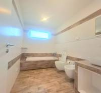 | 4 izbový rodinný dom s krbom a terasov | Slnečná | Ružindol - Kúpeľňa v rodinnom dome s vaňou a toaletou, podlaha s dreveným dekorom.