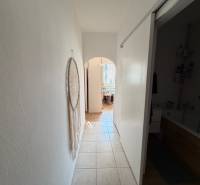 Predaj 3.izbového bytu v Ružinove v obkolesené borovicového lesíka - Chodba s dlažbou v 3-izbovom byte s dekoráciou na stene a pohľadom do kúpeľne.