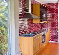 Rodinný dom s veľkou záhradou - Ružinov  - Kuchyňa v Rodinnom dome s červenými obkladmi, drevenými skrinkami a podlahou s dreveným dekorom.