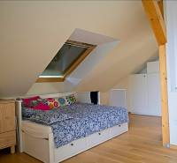 Rodinný dom s veľkou záhradou - Ružinov  - Podkrovná spálňa v rodinnom dome s posteľou, komodou, strešným oknom a podlahou s dreveným dekorom.