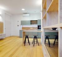 | Butiková 1,5i rezidencia s balkónom | Historická mestská - Svetlý interiér 2-izbového bytu s kuchyňou, podlahou s dreveným dekorom a barovými stoličkami.