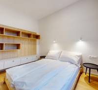 | Butiková 1,5i rezidencia s balkónom | Historická mestská - Spálňa v 2-izbovom byte s posteľou, nástennou policou a podlahou s dreveným dekorom.