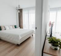 | E2Tower | 20.poschodie | 2i byt | panoramatický výhľad |  - Svetlá spálňa v 2-izbovom byte s posteľou a podlahou s dreveným dekorom.