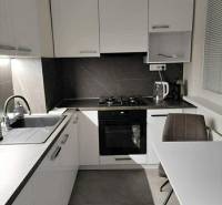 NA PREDAJ ŠTÝLOVÝ 2- IZBOVÝ BYT, 50m2, SÍDLISKO 2, PREŠOV - Kuchyňa s bielymi skrinkami a stolom v 2-izbovom byte s podlahou s dreveným dekorom.