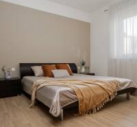 VEĽKÝ ZARIADENÝ 2IB PO KOMPLETNEJ REKONŠTRUKCII - Spálňa v 2-izbovom byte s podlahou s dreveným dekorom, veľkou posteľou a oknom s jemným závesom.