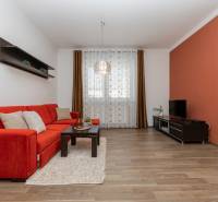 VEĽKÝ ZARIADENÝ 2IB PO KOMPLETNEJ REKONŠTRUKCII - Obývačka s oranžovou sedačkou, poličkami a podlahou s dreveným dekorom v 2-izbovom byte.