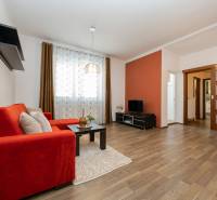 VEĽKÝ ZARIADENÝ 2IB PO KOMPLETNEJ REKONŠTRUKCII - Obývačka v 2-izbovom byte s pohovkou, TV, podlahou s dreveným dekorom a dekoratívnymi závesmi.