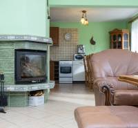 RD s VEĽKÝM POZEMKOM V SRDCI PRÍRODY, Tŕstie - Interiér rodinného domu s krbom, sedacou súpravou a kuchynským kútom v prírodných odtieňoch.