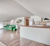 4-izbový podkrovný byt s nebytovým priestorom v obci Pavlice - Obývacia izba s kuchyňou, zelená sedačka, biely nábytok, podlaha s dreveným dekorom.