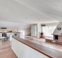 4-izbový podkrovný byt s nebytovým priestorom v obci Pavlice - Obývacia izba s krbom a kuchynskou časťou, podlaha s dreveným dekorom, svetlá miestnosť.