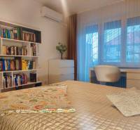 Vkusný, moderný 2 izb, klíma, 870 s ener., Sibírska ul./Nové Mesto - Spálňa v 2-izbovom byte s posteľou, poličkami plnými kníh a pracovným stolom.