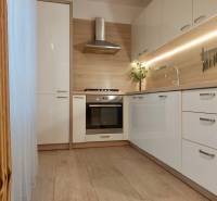 Vkusný, moderný 2 izb, klíma, 870 s ener., Sibírska ul./Nové Mesto - Kuchynská linka v 2-izbovom byte s podlahou v drevenom dekore a závesmi.