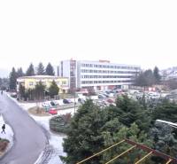 Predaj 2 - izbového bytu v Banskej Štiavnici - Zasnežený výhľad na ulicu Bratská v meste Banská Štiavnica obklopenú budovami a zeleňou.