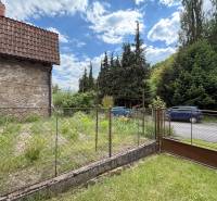 Predaj domu v Janovej Lehote - Kamenná stena rodinného domu v Janovej Lehote, pri ceste s autami a zeleňou.