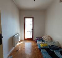 : Predaj rodinného domu s veľkým pozemkom v obci Pitelová  - Izba v rodinnom dome s radiátorom, jednoduchým lôžkom a podlahou s dreveným dekorom.