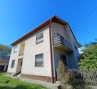 : Predaj rodinného domu s veľkým pozemkom v obci Pitelová  - Rodinný dom v Pitelovej s balkónom a záhradou, modrá obloha, plot a zeleň.